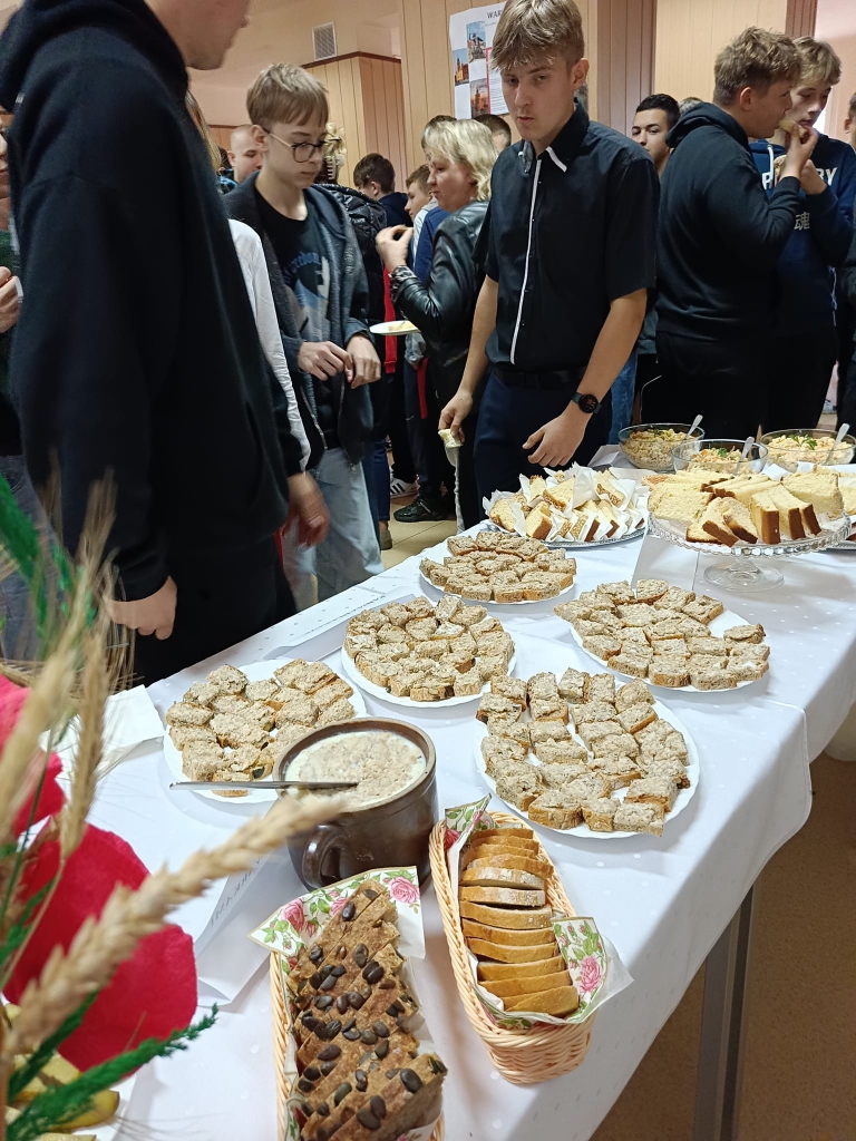 Na stole stoją talerze z ciastem, salaterka ze smalcem, chleb. Obok stołu stoi młodzież